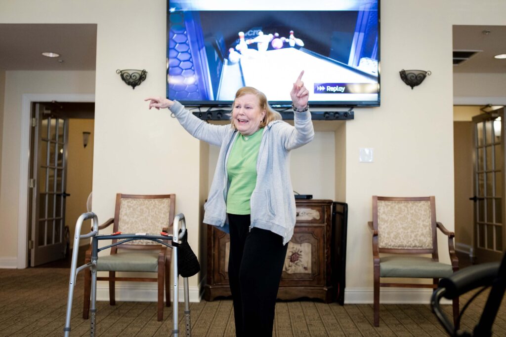 Grace_Management_Memphis_2018-4107 - Northgate Park An older woman lifting her hands in the air as she's turned away from the TV, which displays a strike in the video game of bowling at Northgate Park.