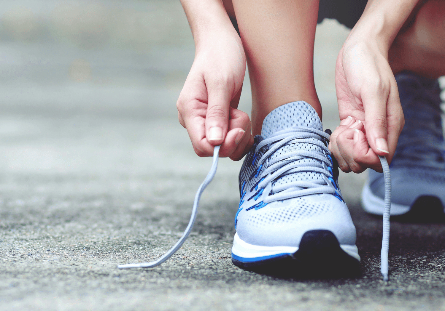 Person tying the laces of a light blue athletic shoe on the ground, preparing to run